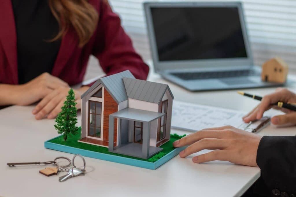 A man and woman discuss a model house at a table