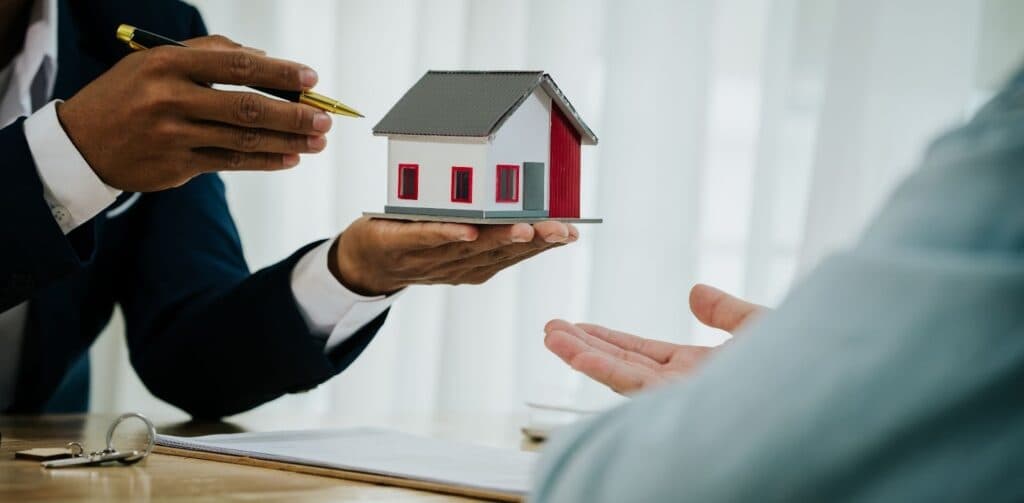 Real estate agent handing house keys and model home to buyer over contract.