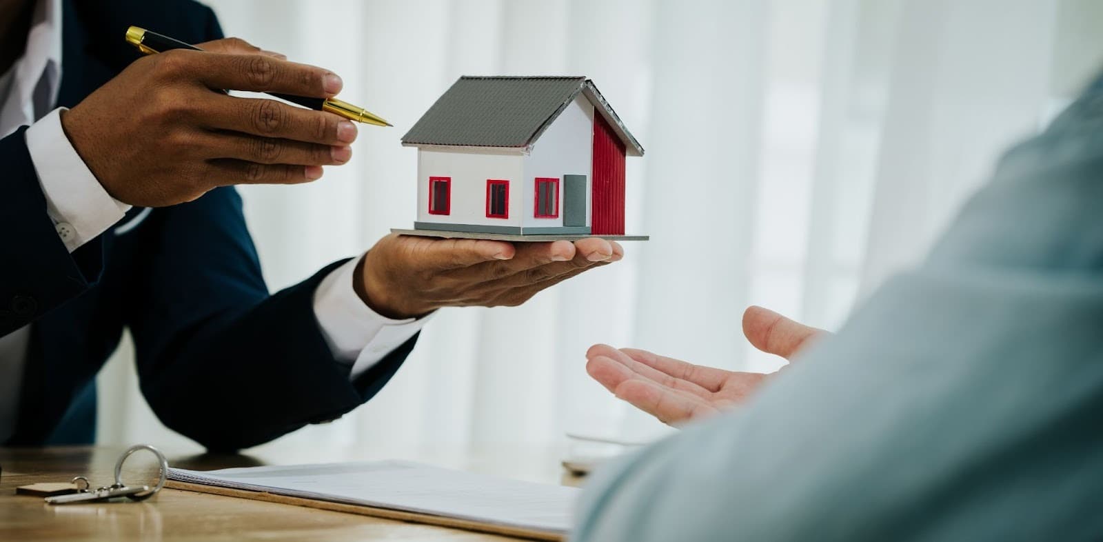 Real estate agent handing house keys and model home to buyer over contract.